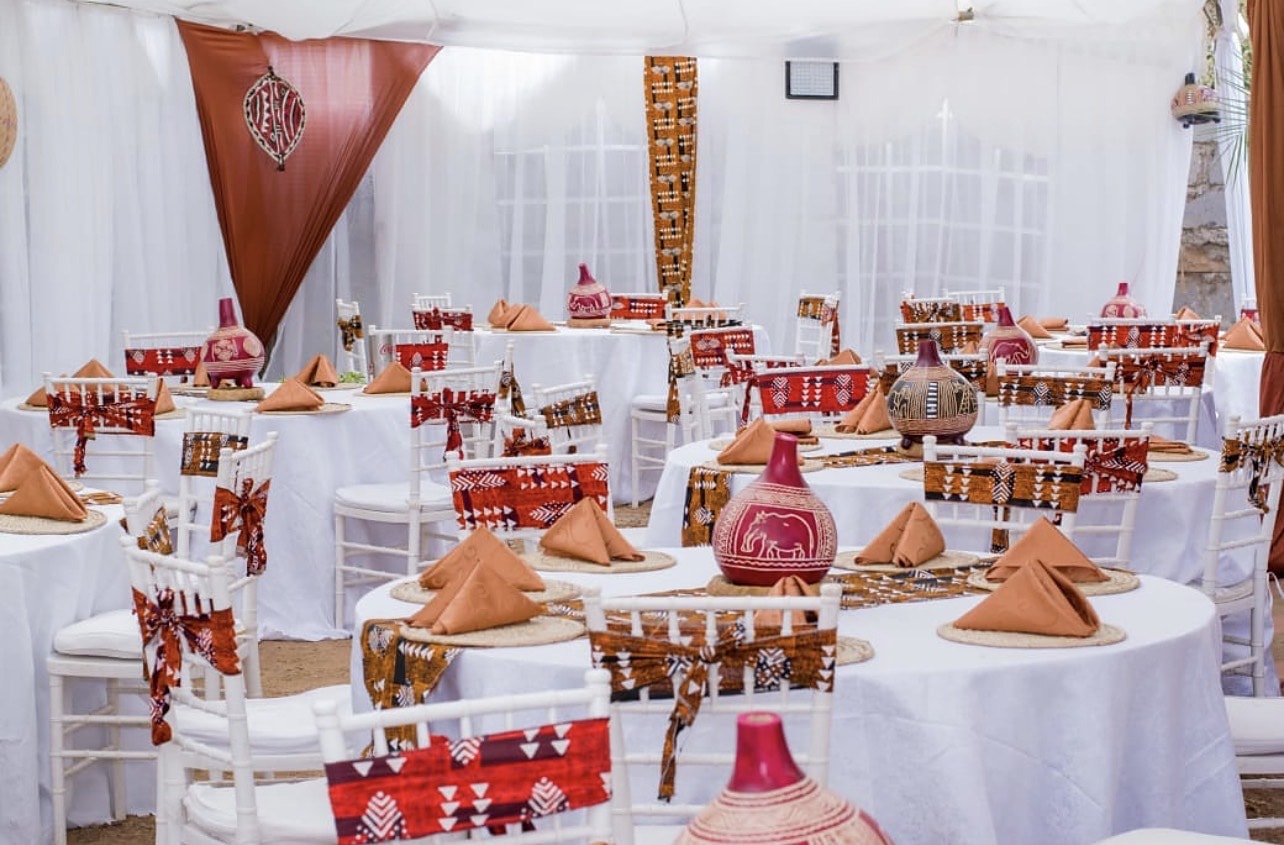 Round tables with African-print runners and chair sashes, terracotta napkins and painted gourds