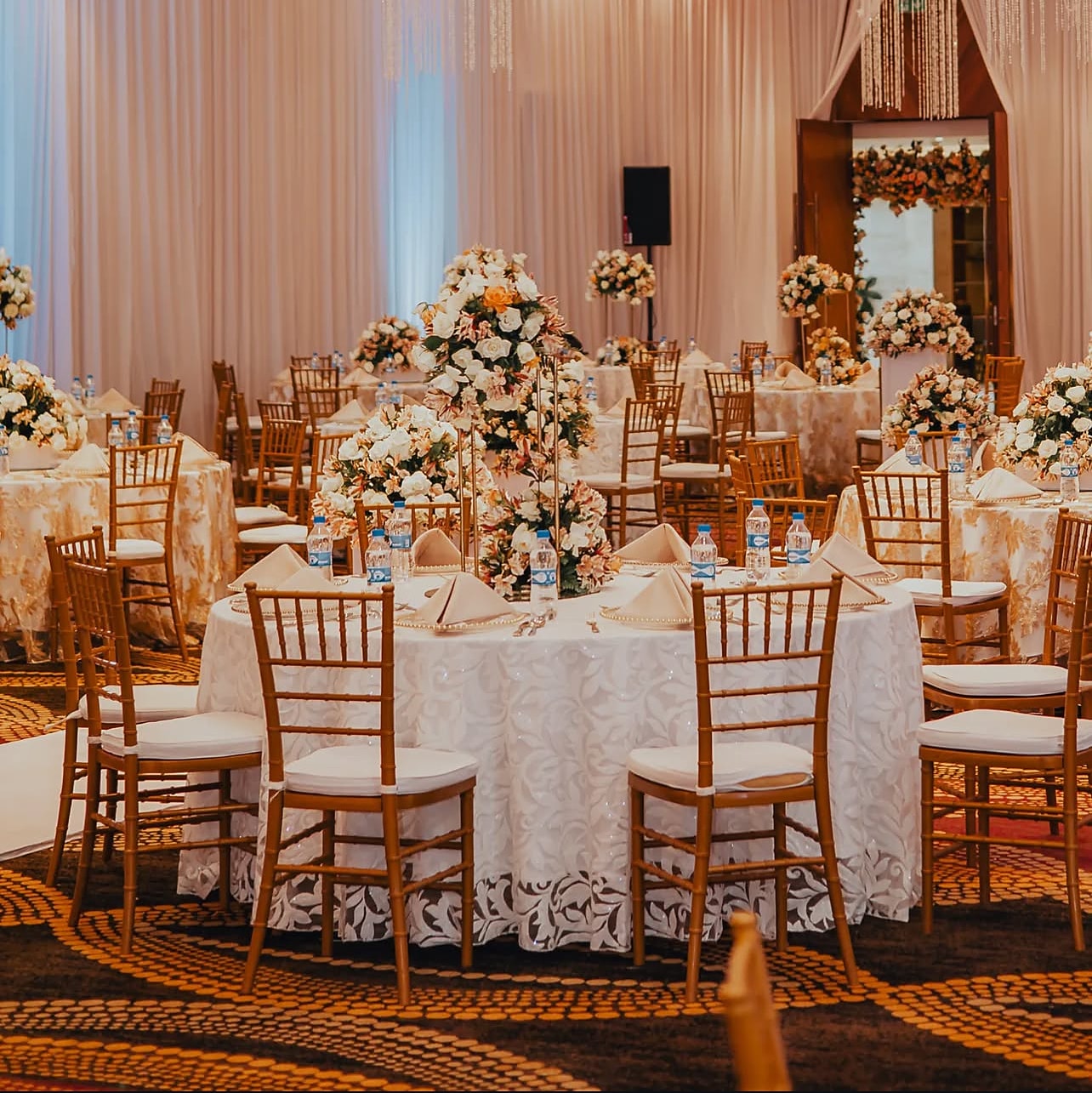 Ballroom round tables in lace linens with gold chairs and red and ivory rose centrepieces