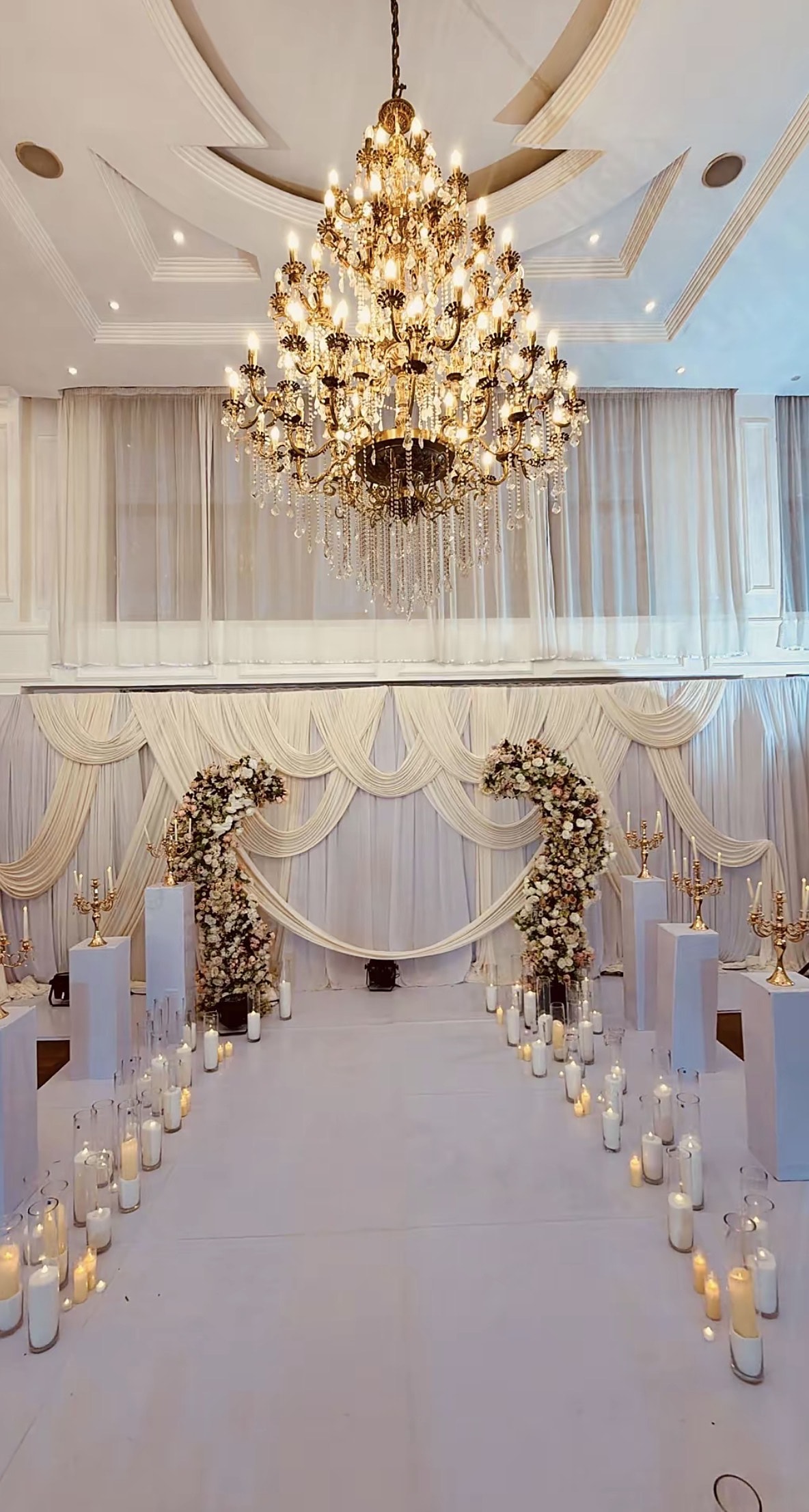 Candlelit aisle under a crystal chandelier with gold floral stands