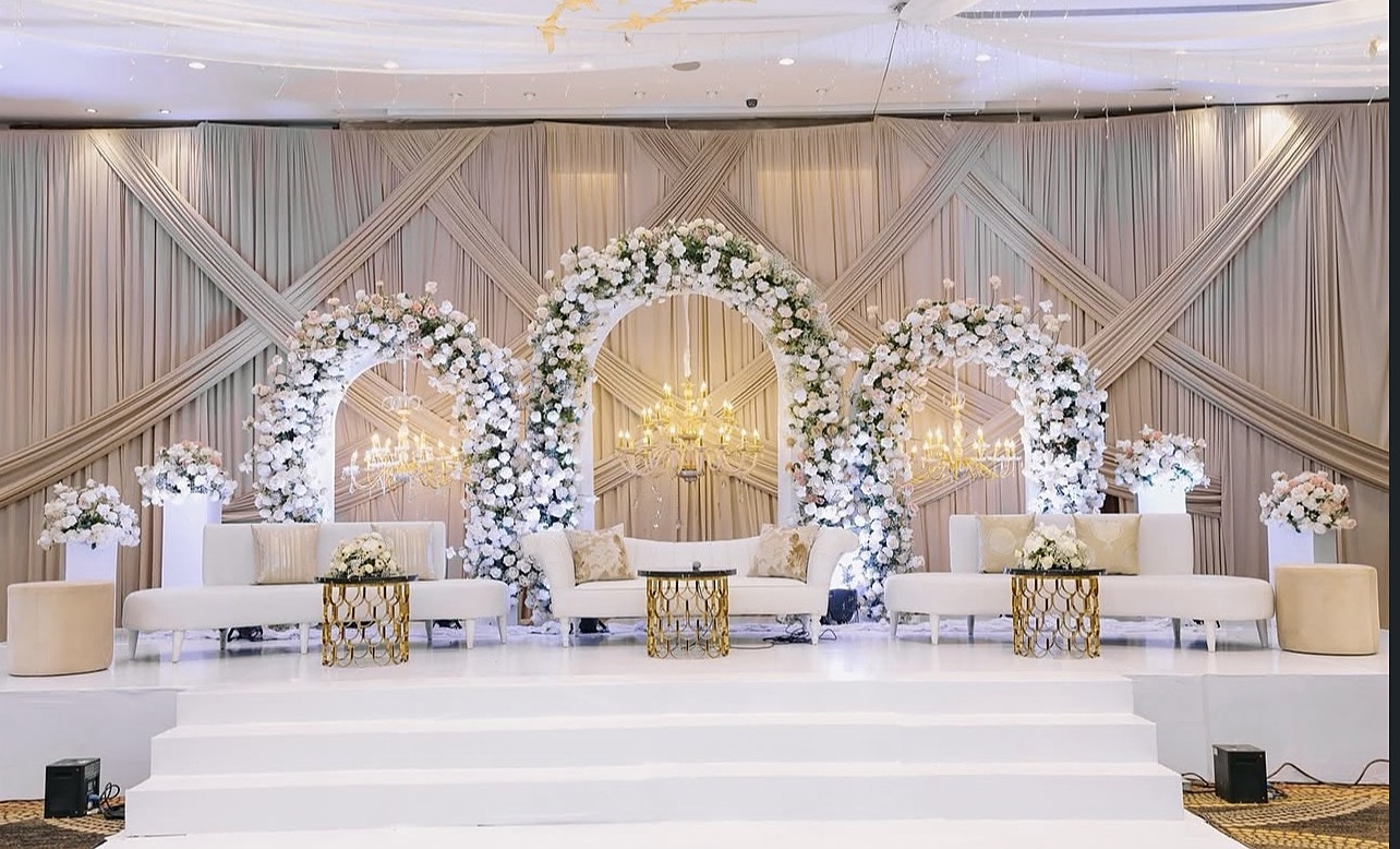 Stage with three white floral arches, ivory sofas and gold side tables