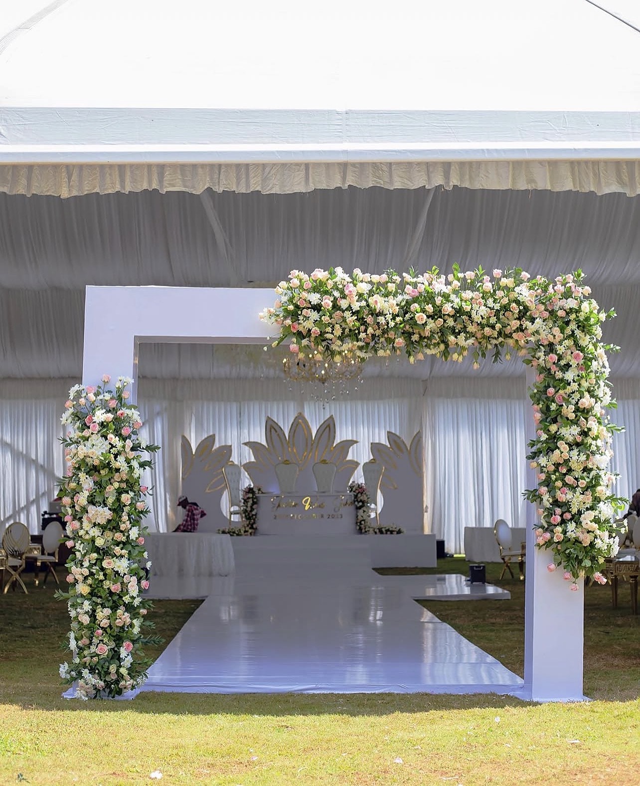 Floral gateway opening onto a white stage inside a marquee