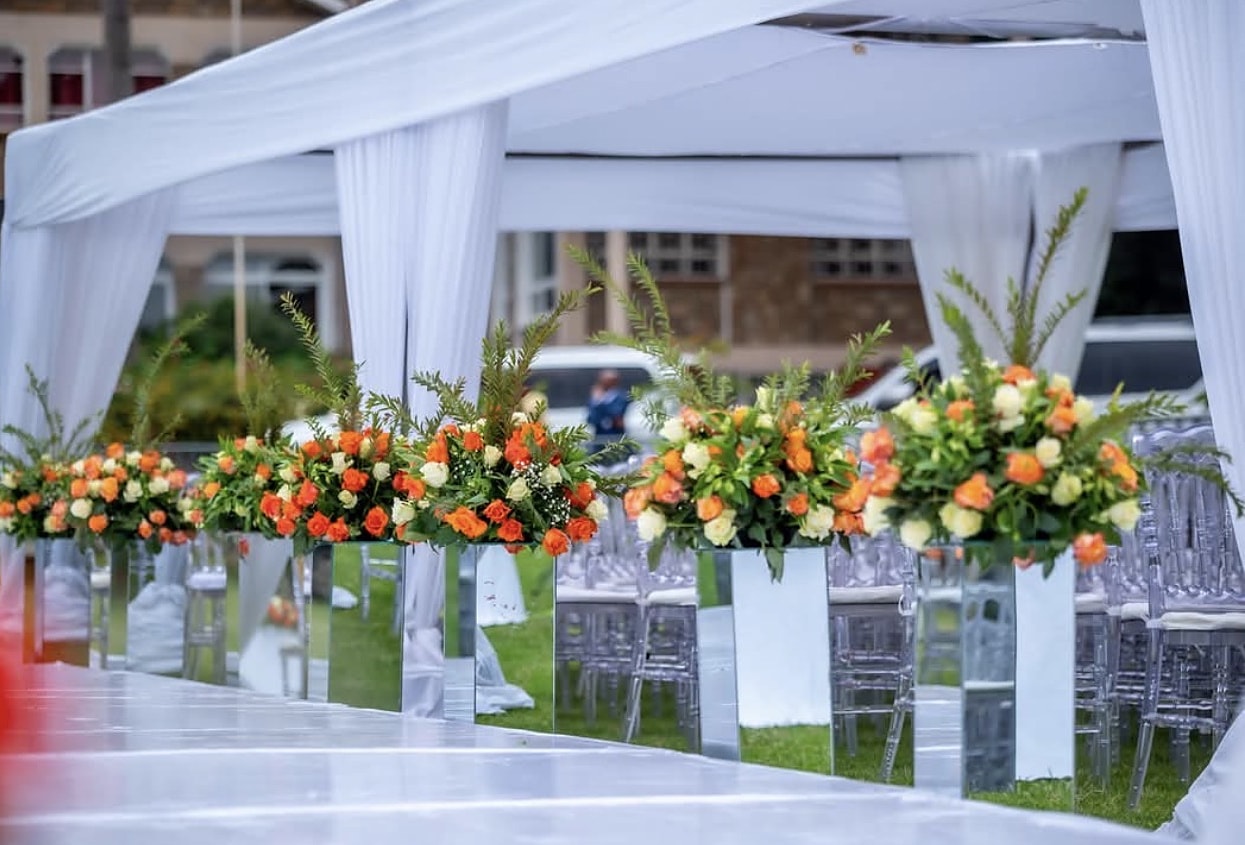 Mirrored plinths with orange and white florals lining a white aisle under a garden marquee