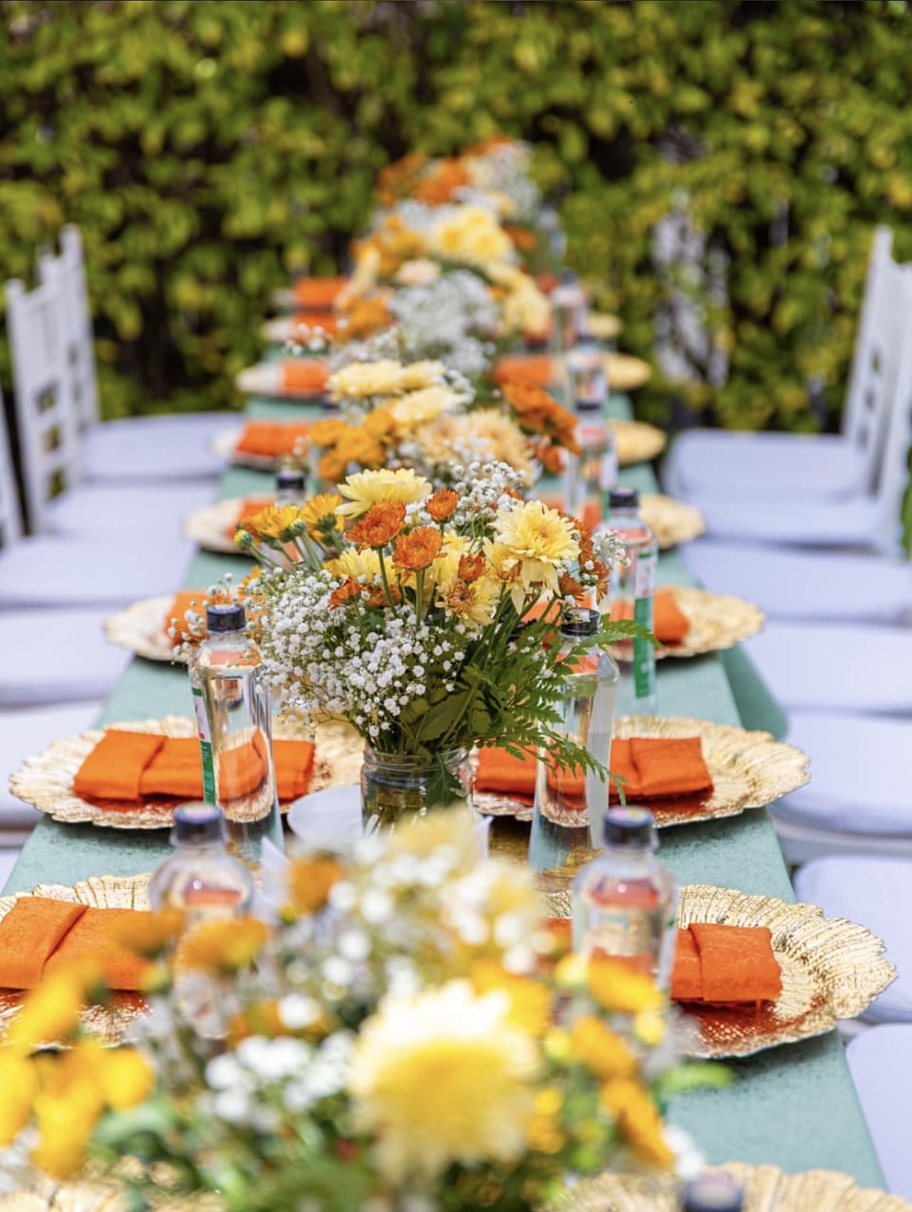 Long garden table with gold chargers, orange napkins and yellow and orange flowers