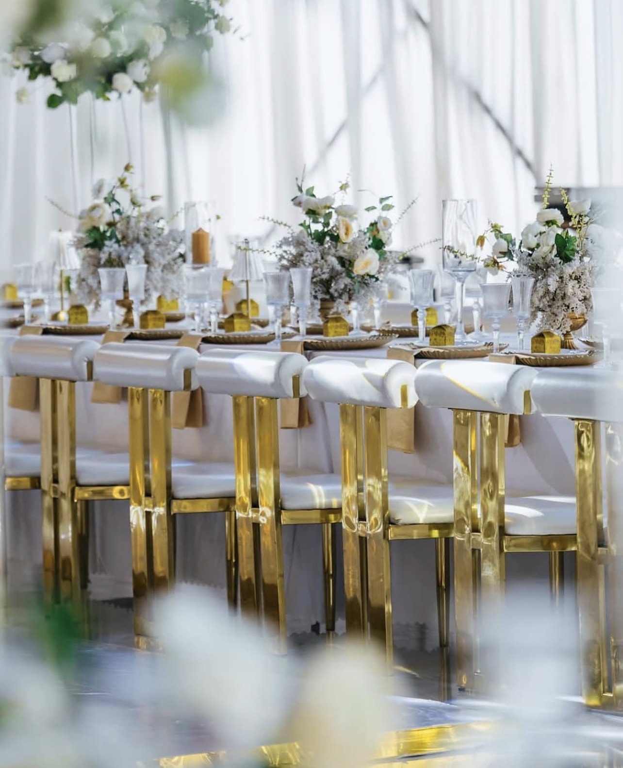 Long table with gold-framed white chairs and white floral centrepieces