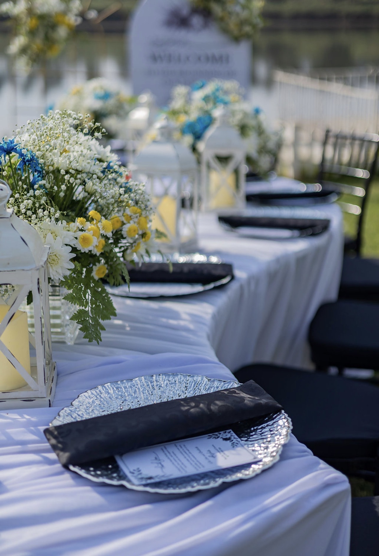 Dinner table with silver chargers, lanterns and white and yellow flowers