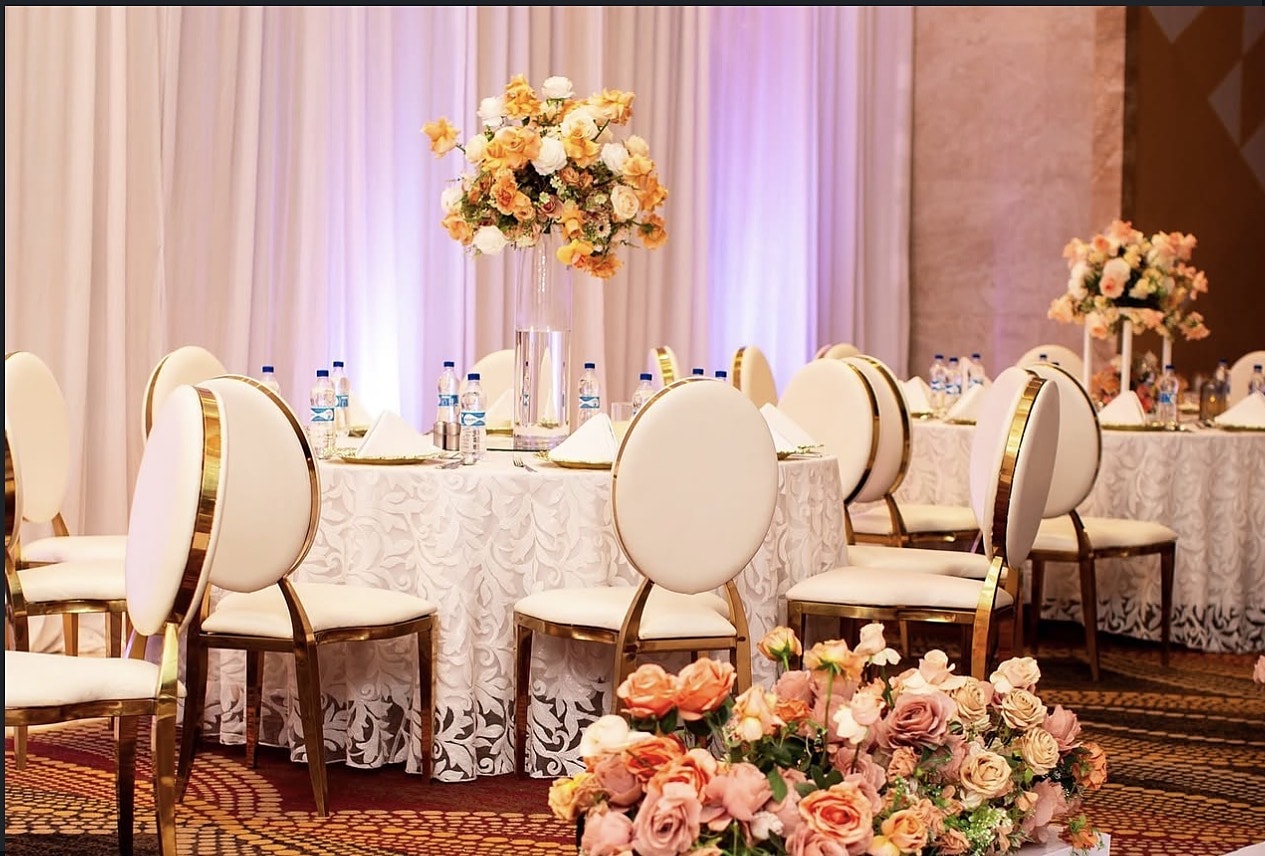 Round tables with white and gold chairs and low peach rose arrangements