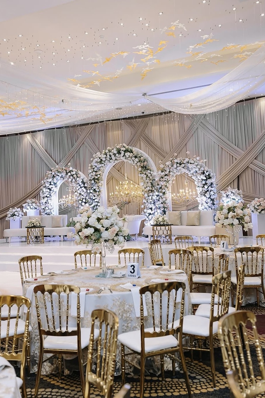Ballroom with white floral arches behind the head table and gold chairs