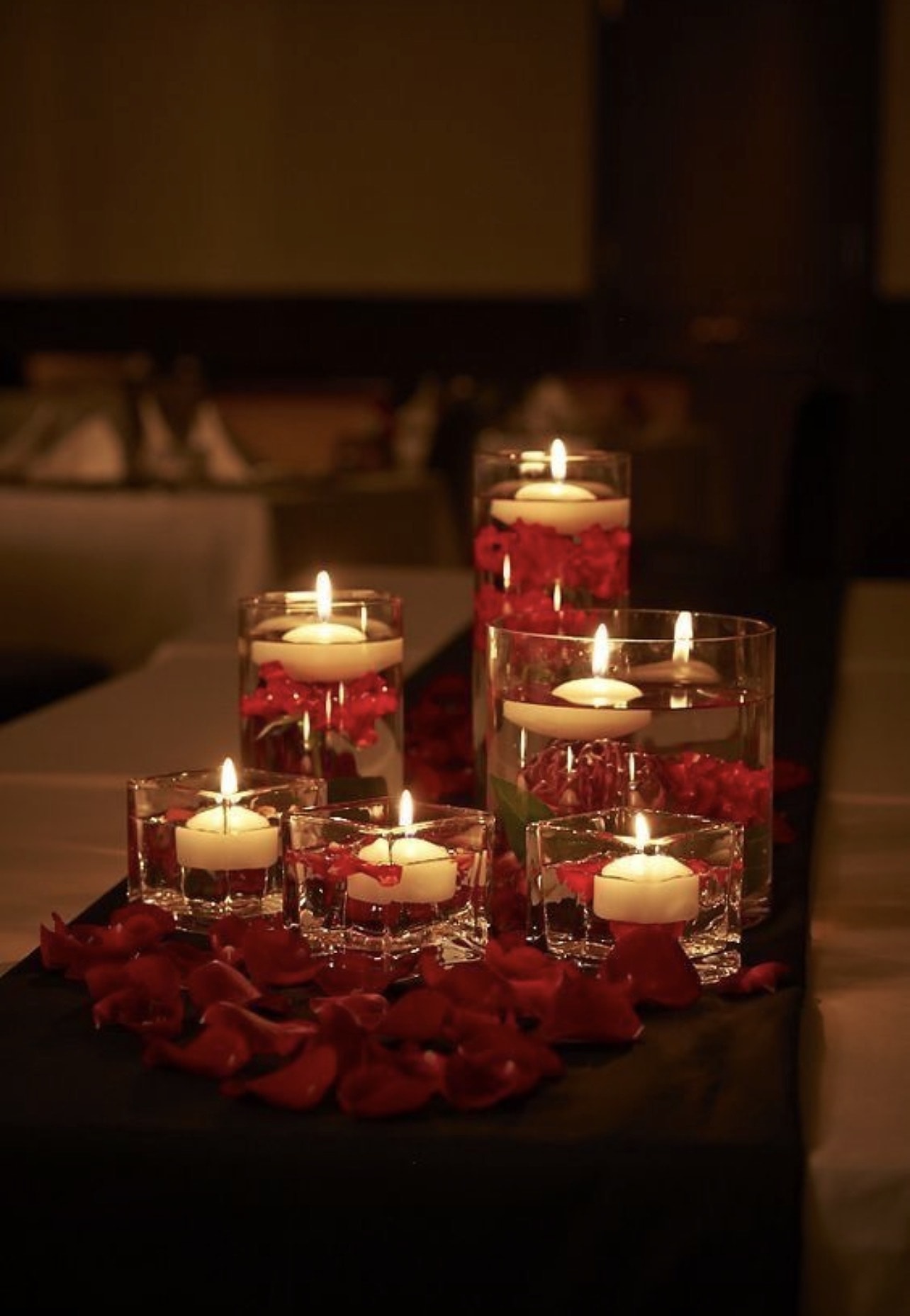 Floating candles in glass vases surrounded by red rose petals
