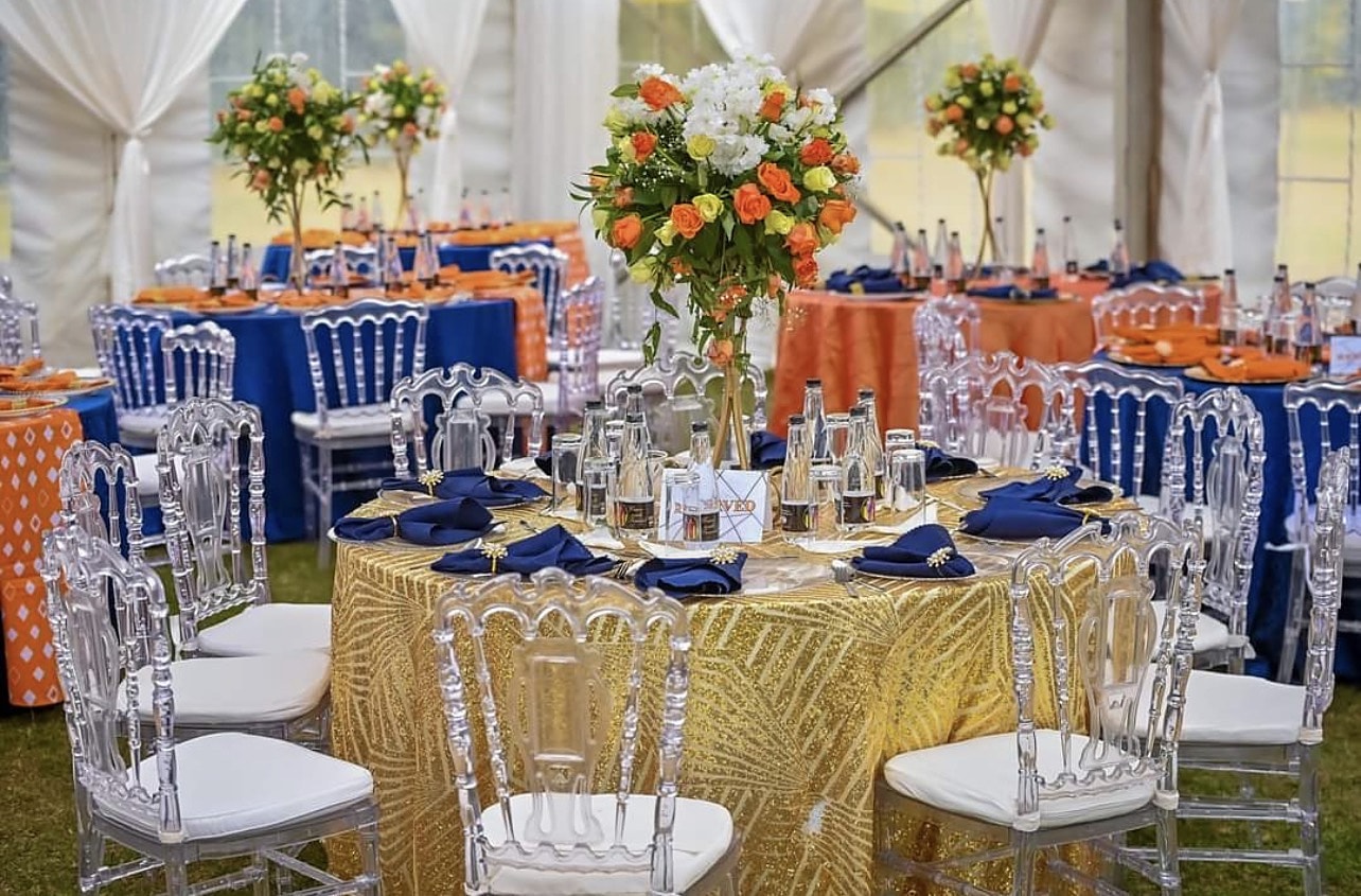 Round tables in gold sequin and cobalt linens with tall orange floral centrepieces