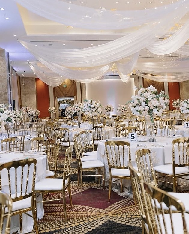 Gold chairs and round tables before white floral arches in a ballroom