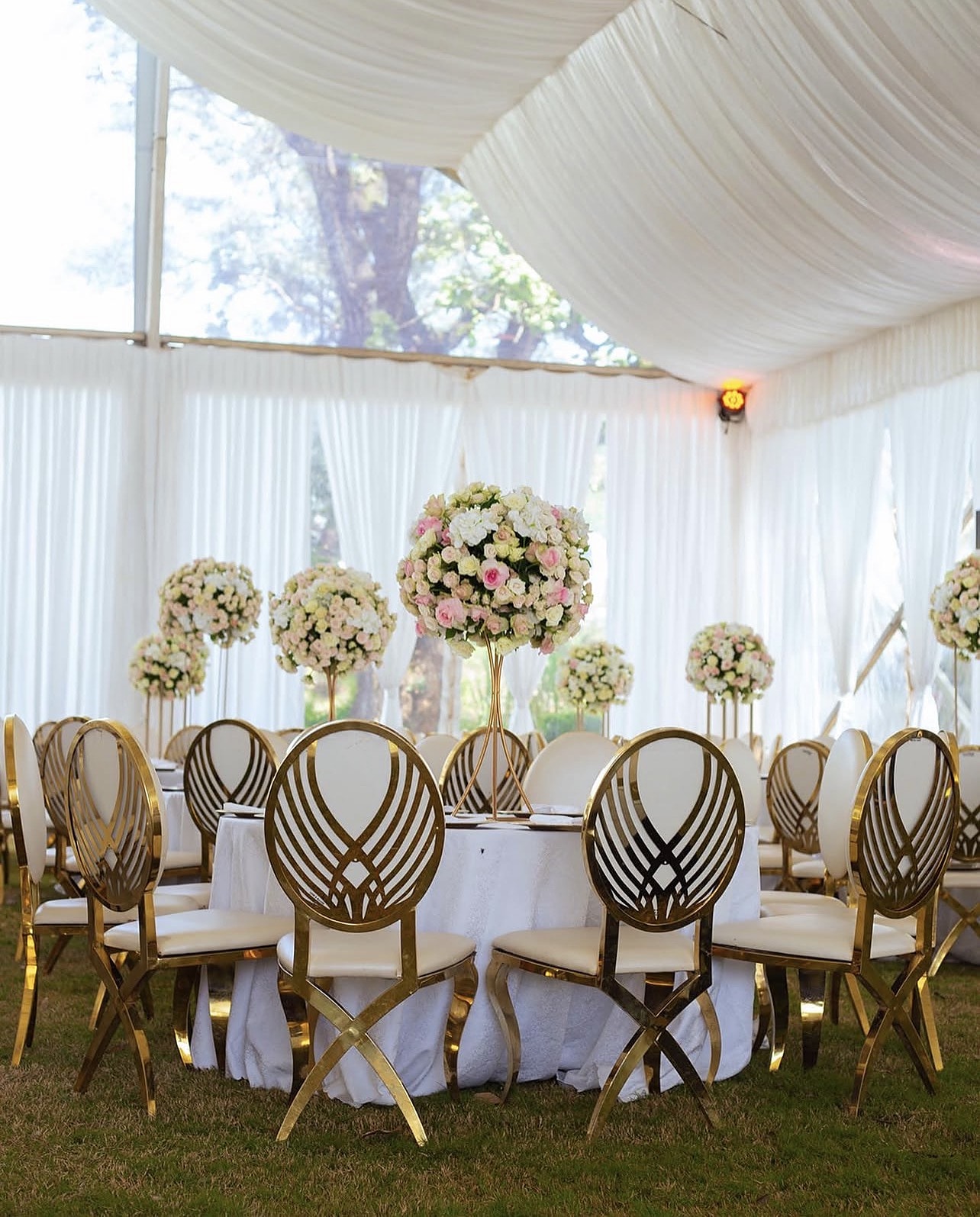 Round tables with tall pink floral centrepieces and gold chairs under a white marquee