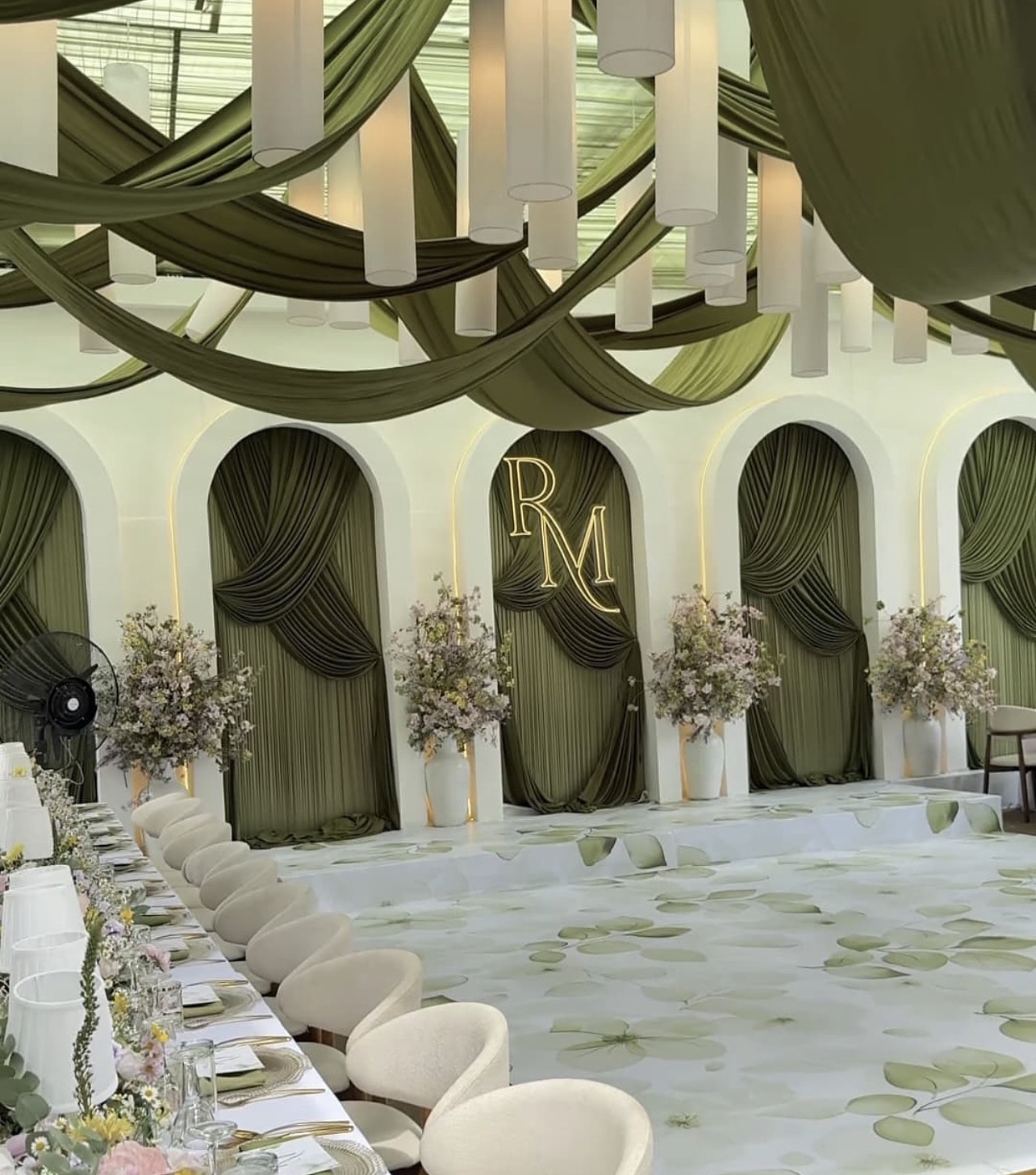 Long table set before a row of olive-green draped arches