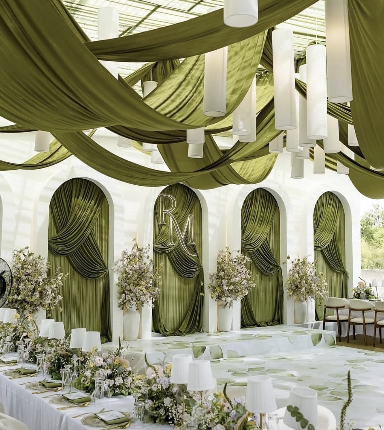 Reception with olive-green draped arches, white lanterns and low floral runners