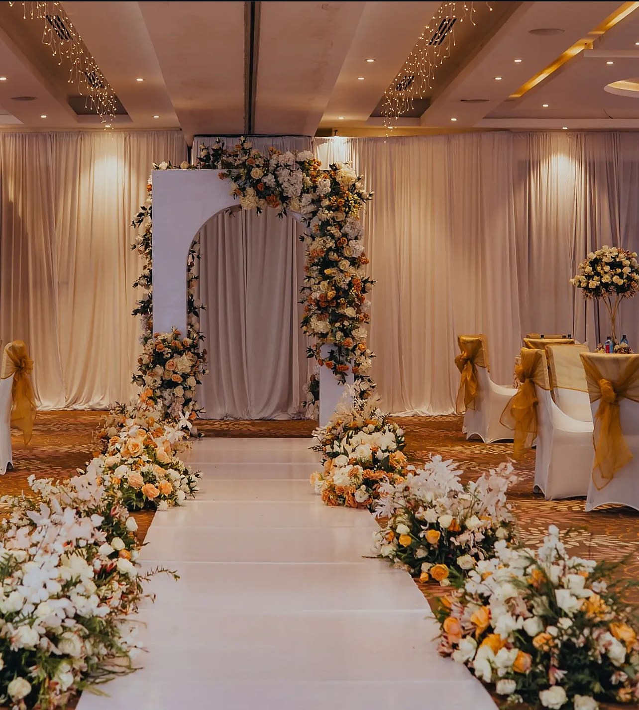 White aisle through peach and ivory florals to a floral arch in a ballroom