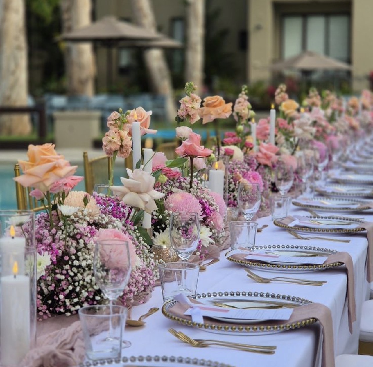 Poolside long table with blush roses, candles and gold cutlery