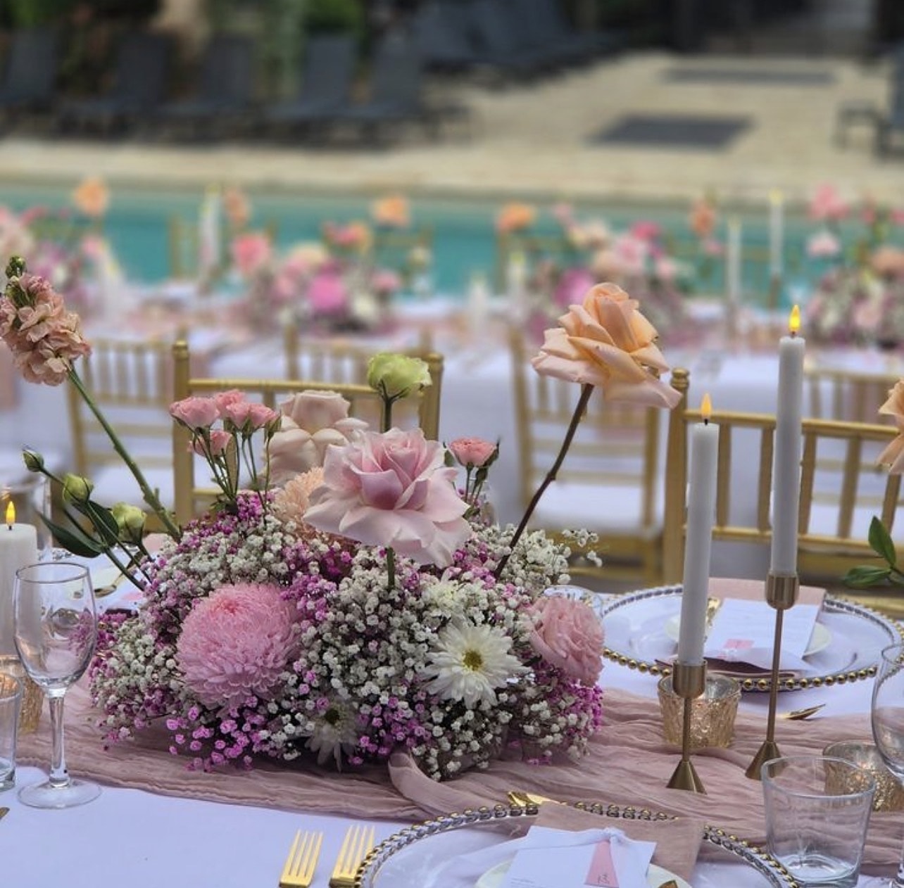 Close-up of a pink floral centrepiece with taper candles by a pool