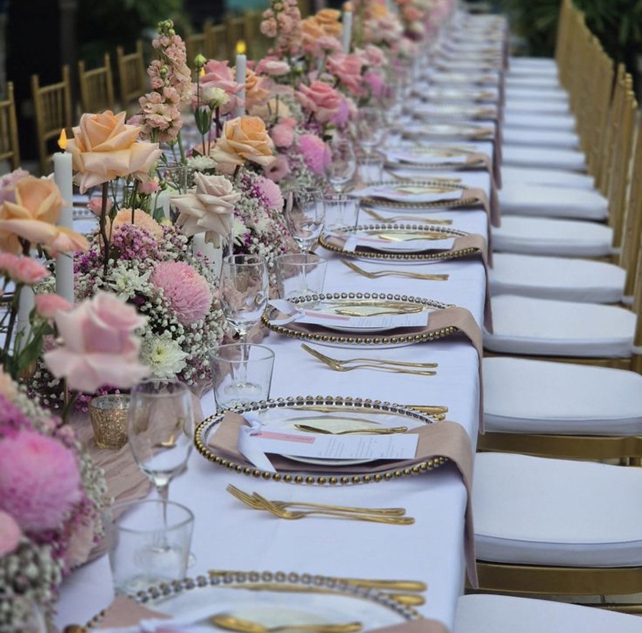 Beaded gold chargers, menu cards and pink florals along a poolside table