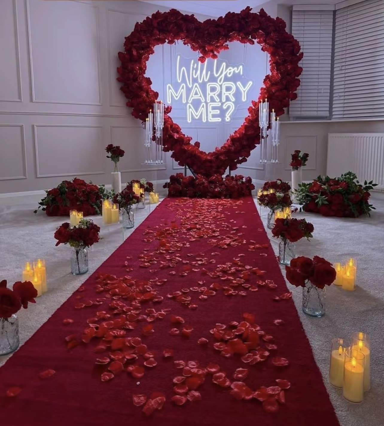 Proposal set-up with a red rose heart, neon sign and petal aisle lined with candles