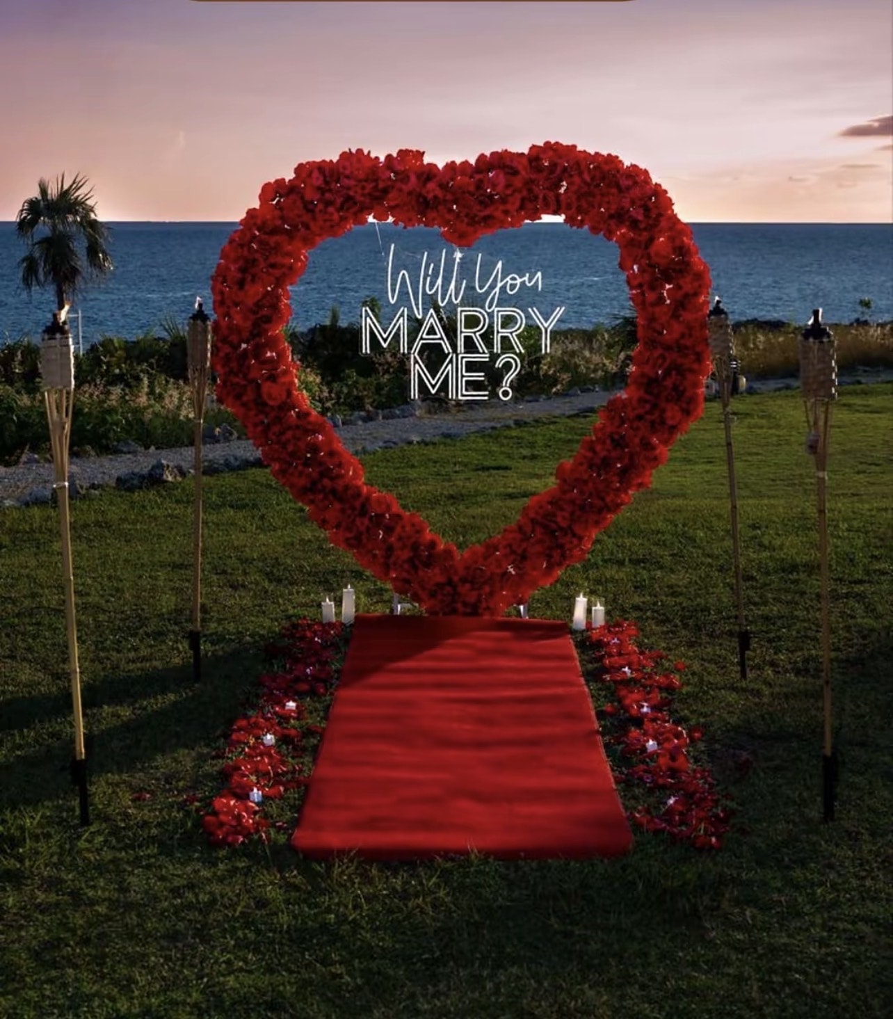 Red rose heart with a Will You Marry Me neon on a seaside lawn at dusk