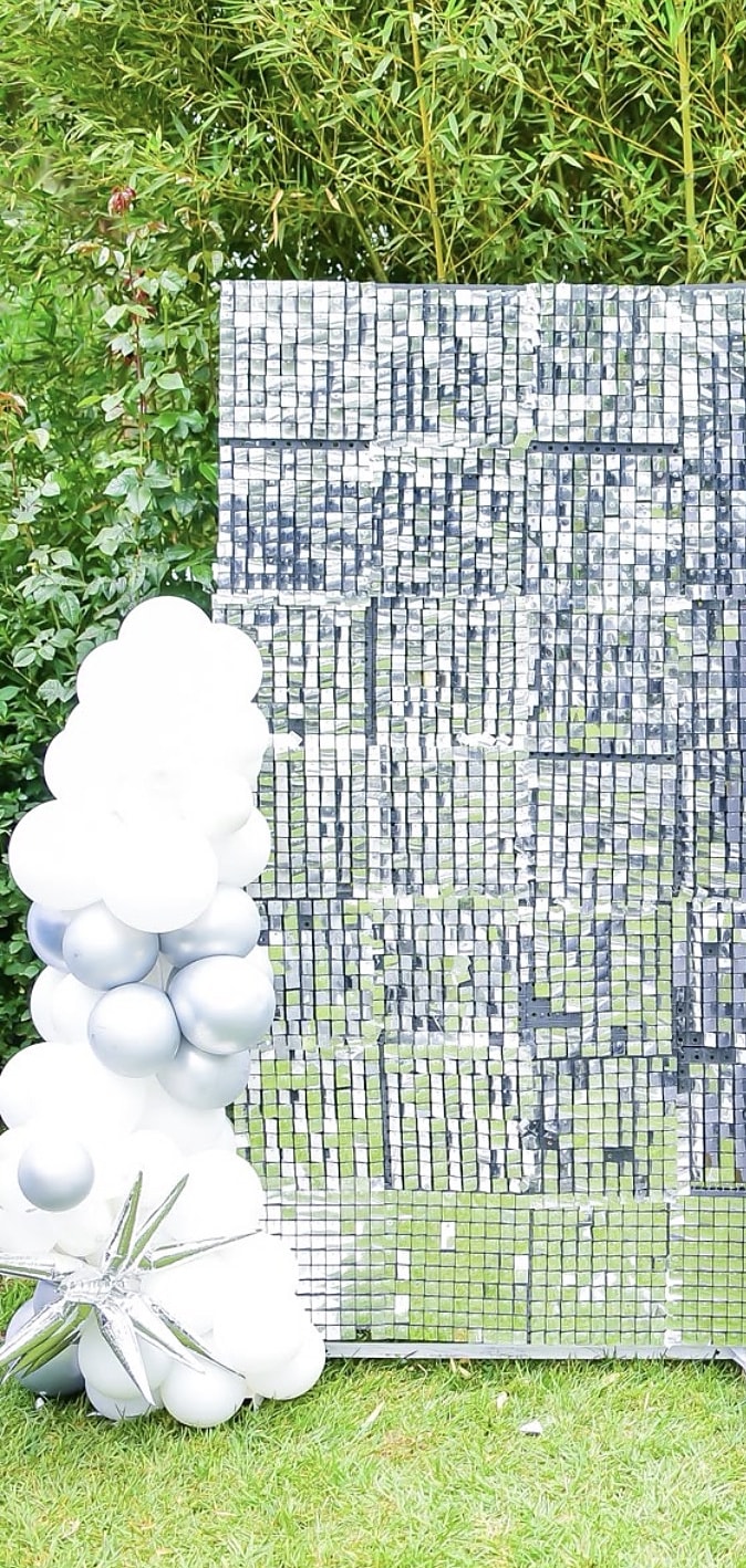 Silver sequin photo wall framed by white and silver balloons on a lawn